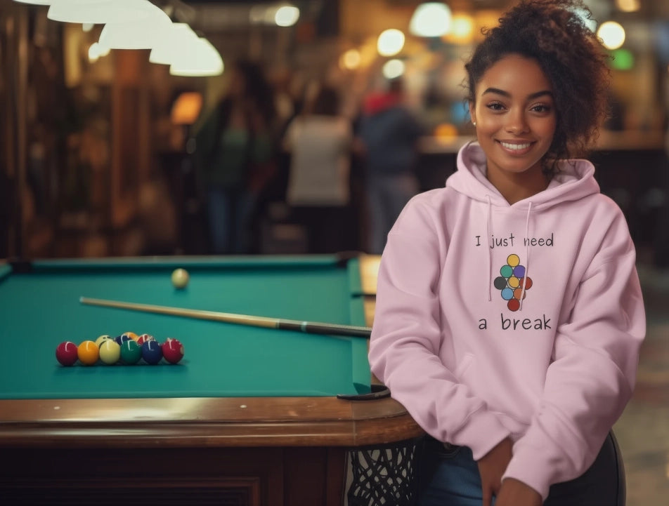 Woman in pink hoodie with colorful design and text, sitting next to a pool table.