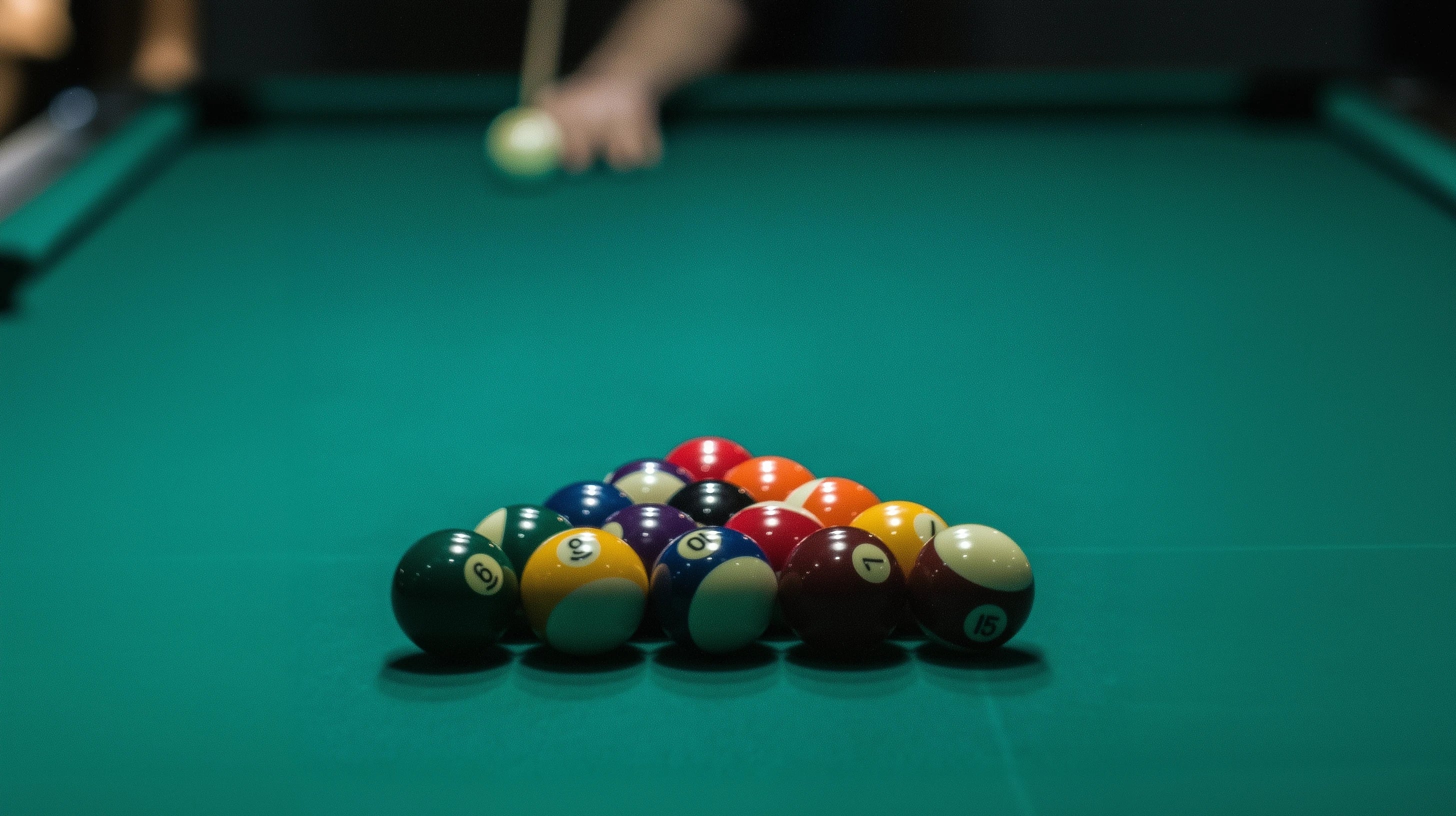 Rack of 15 billiard balls with a pool player in the background about to shoot