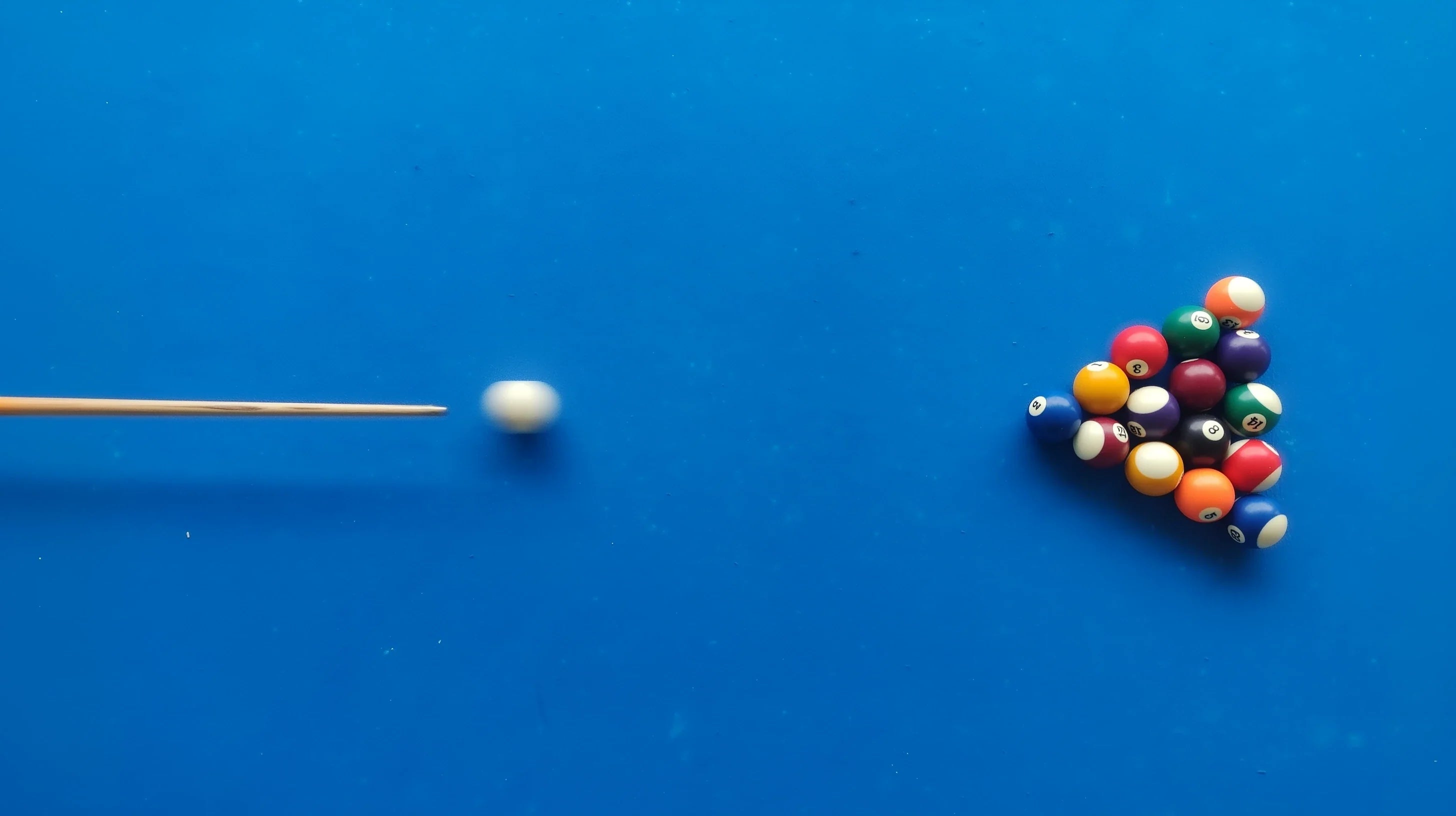 A rack of balls on a blue cloth table moments before break shot impact from the cue ball
