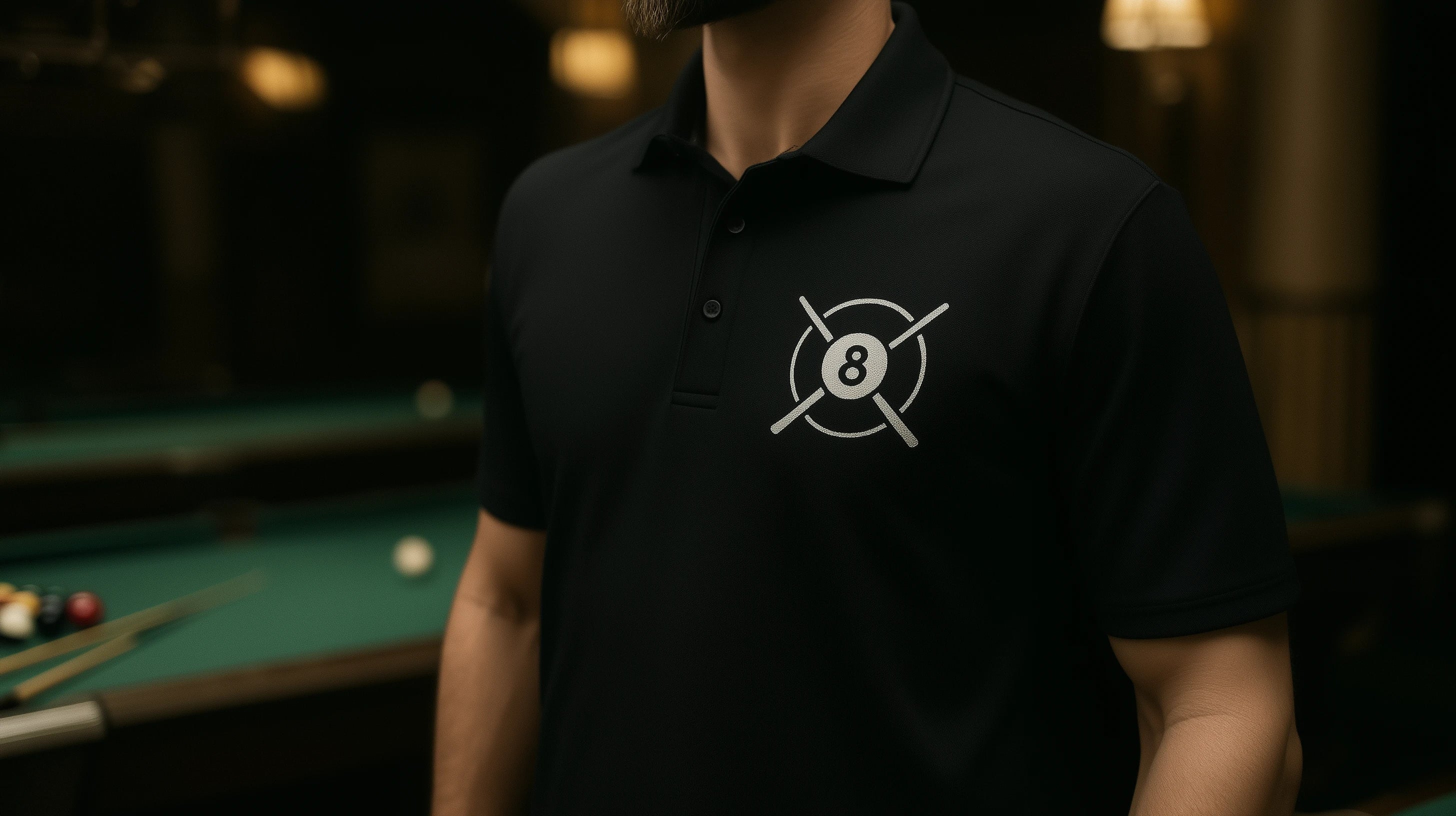 A man standing in a pool hall wearing a black polo shirt with an eight ball logo on it
