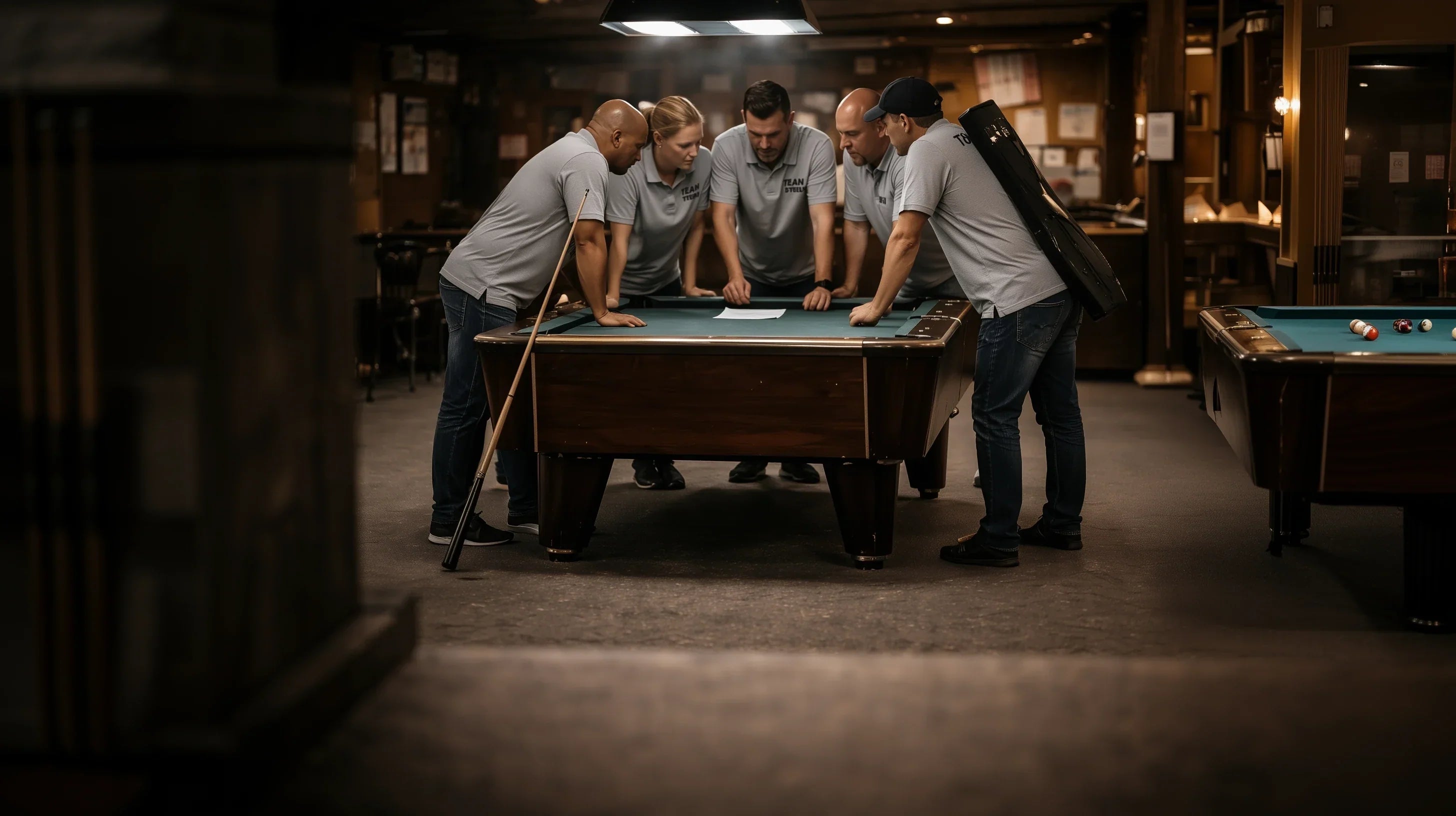 A pool team wearing matching grey shirts standing around a pool table discussing strategy